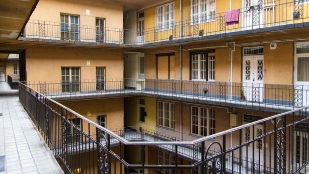 Een meerlaags woongebouw met balkons, hekken en een betegeld gelijkvloers.