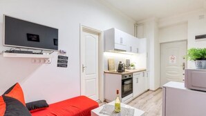 Een knus verblijf met kitchenette, een wandgemonteerde flatscreen-tv, een rode bank en een kleine tafel met fles en glazen.