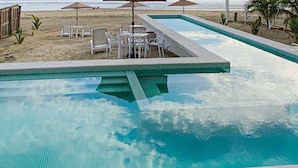 Una piscina con borde de baldosas, rodeada de sillas y mesas de descanso.