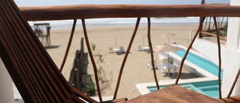 A wooden chair and table with a view of a beach and a pool.