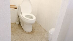 A small, white toilet in a corner with a plain wall and a speckled floor.