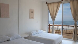 A room with two beds, a beach view, and a wooden deck.