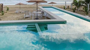 A swimming pool with a tiled deck, surrounded by lounge chairs and tables. - Junior Suite Apartment (Zihuatanejo)