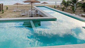 A swimming pool with a tiled deck, surrounded by lounge chairs and tables.