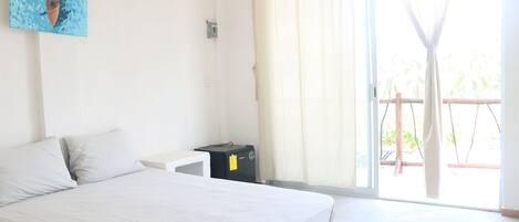 Een slaapkamer met een bed, een klein nachtkastje, een stopcontact en een raam met gordijnen.