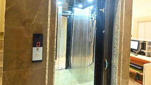 Un ascensor con pantalla digital, interior metálico y suelo de mármol.