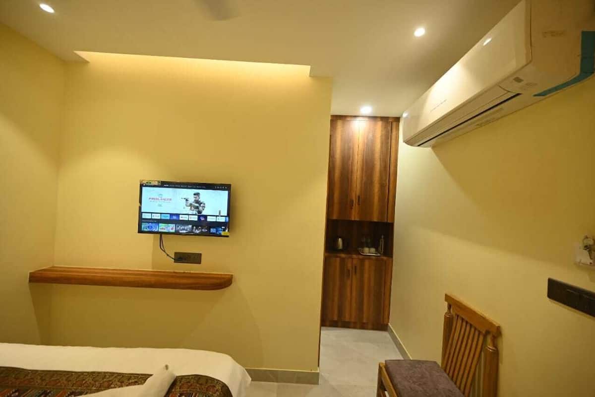 A hotel room with a bed, a television mounted on the wall, a wooden cabinet, and an air conditioning unit.