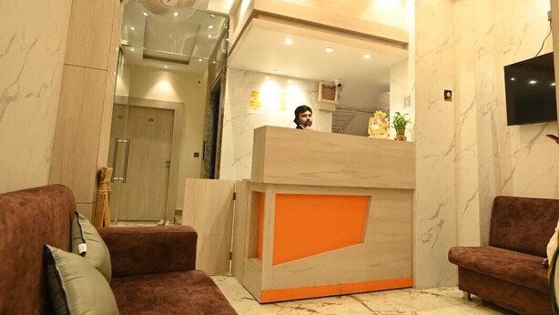 Un vestíbulo moderno con suelo de mármol, una recepción con detalles en naranja y un televisor montado en la pared.