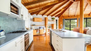 A modern kitchen with a central island, wooden ceiling beams, and a view to the outside. - Hidden Orchard - Pet Friendly - 4 Mins Walk to Beach (Callala Bay)