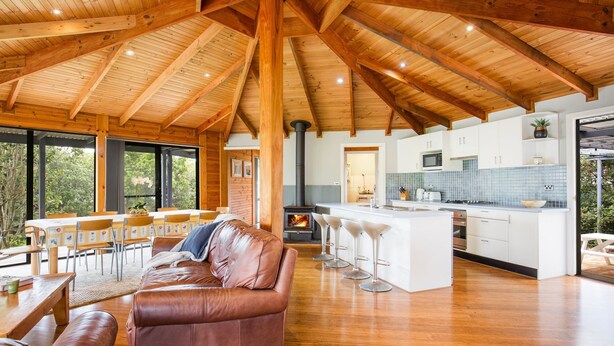 A spacious living area with a wooden ceiling, a leather sofa, a dining table with chairs, and a kitchen with white cabinets and a blue backsplash. - Hidden Orchard - Pet Friendly - 4 Mins Walk to Beach (Callala Bay)
