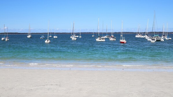 A beach with numerous sailboats anchored in calm waters.