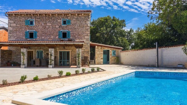 Un edificio de piedra con piscina, mobiliario exterior y cielo azul despejado.