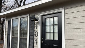 Una casa con puerta principal negra, tres ventanas con contraventanas y el número 101 en la pared.