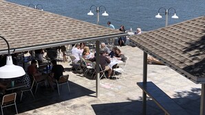 Un área de comedor al aire libre con mesas y sillas, una zona de estar cubierta y vista al agua.