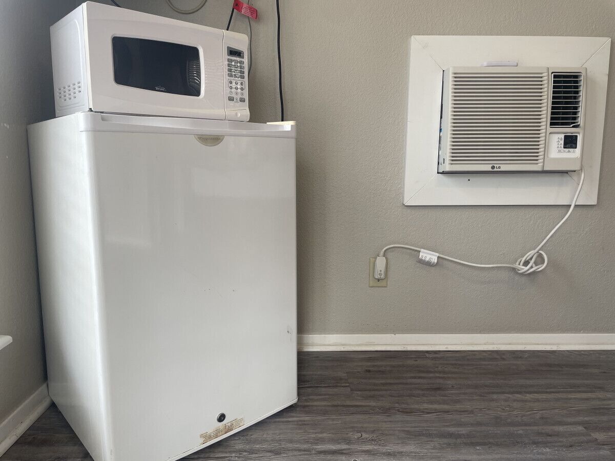 Ein weißer Kühlschrank mit Mikrowelle obenauf, eine Klimaanlage und eine Steckdose an der Wand.
