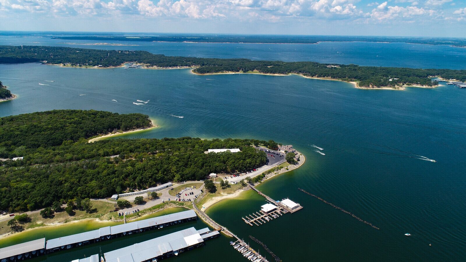 An aerial view of a coastal area with a marina, a dock, and a building with a large roof.