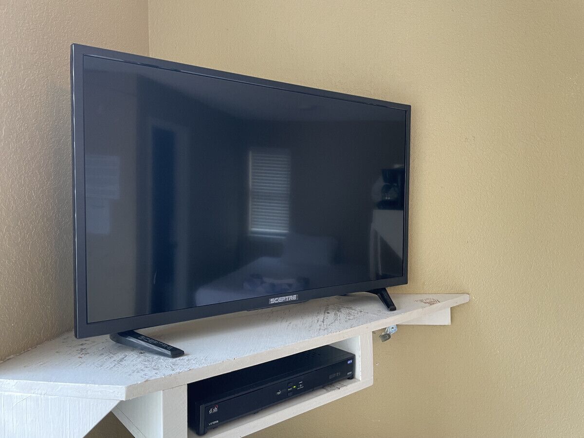Un téléviseur à écran plat fixé sur une étagère blanche, avec un décodeur câblé placé en dessous.