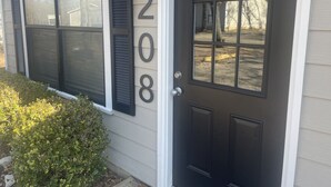 Une maison avec une porte d’entrée noire, le numéro « 208 » sur le mur et une fenêtre avec des volets.