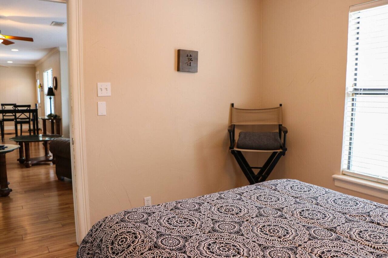 Une chambre à coucher avec une couvre-lit à motifs, une petite table avec une chaise et une étagère fixée au mur.