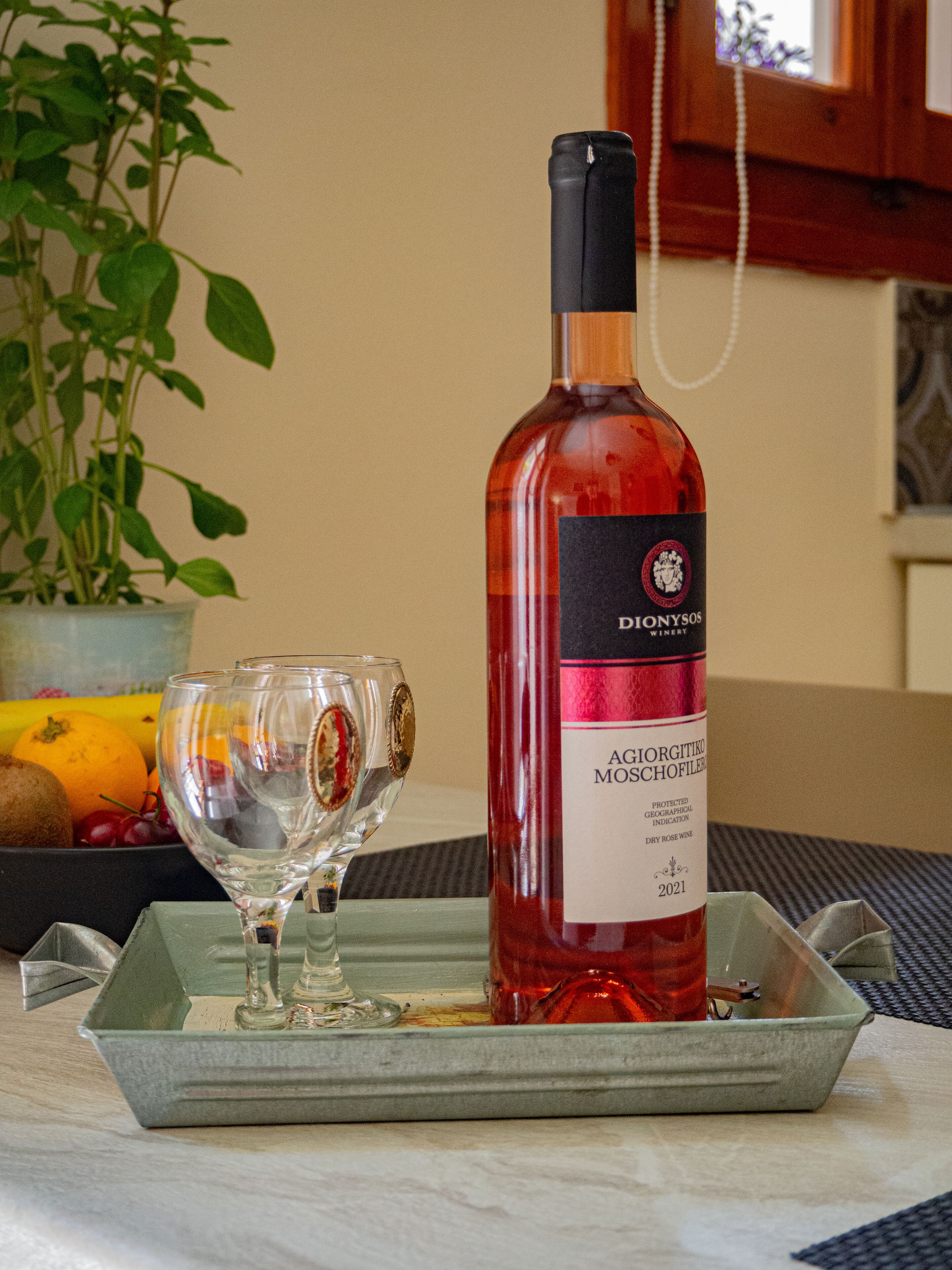 Una botella de vino de la bodega Dionysos sobre una bandeja con una copa y una cesta de fruta.