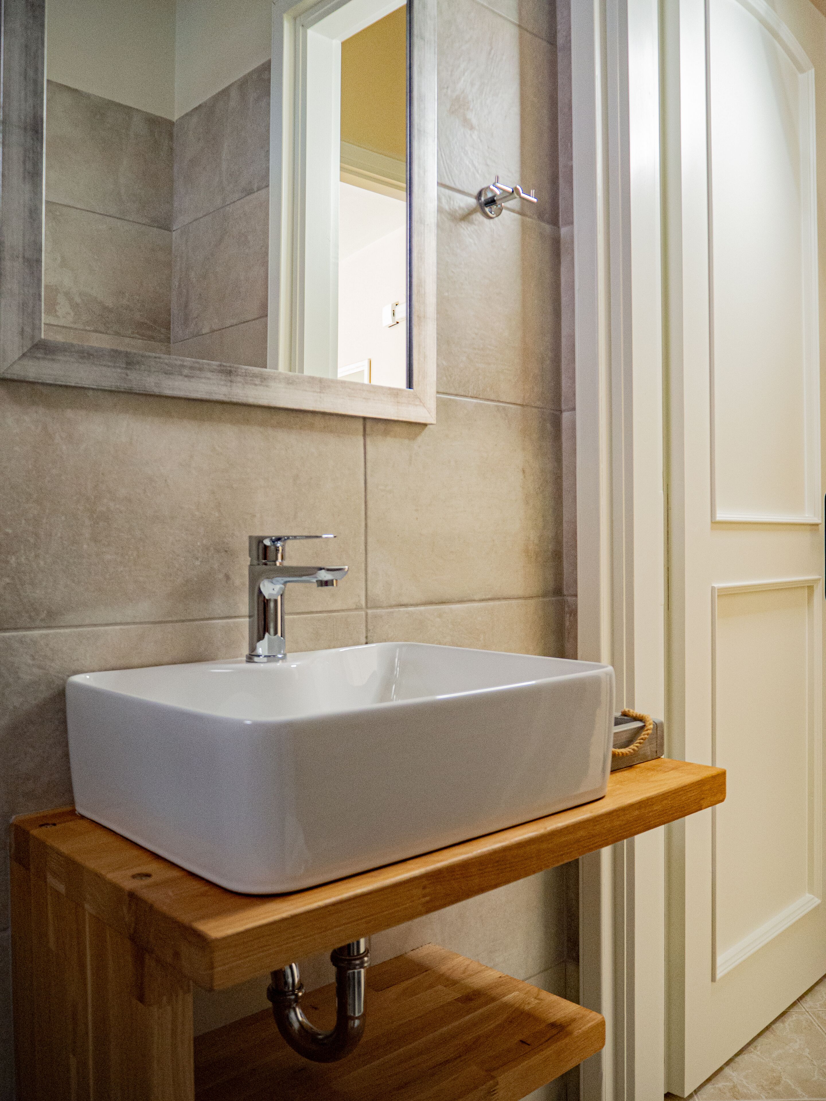Un baño con un lavabo blanco, un estante de madera y un espejo.