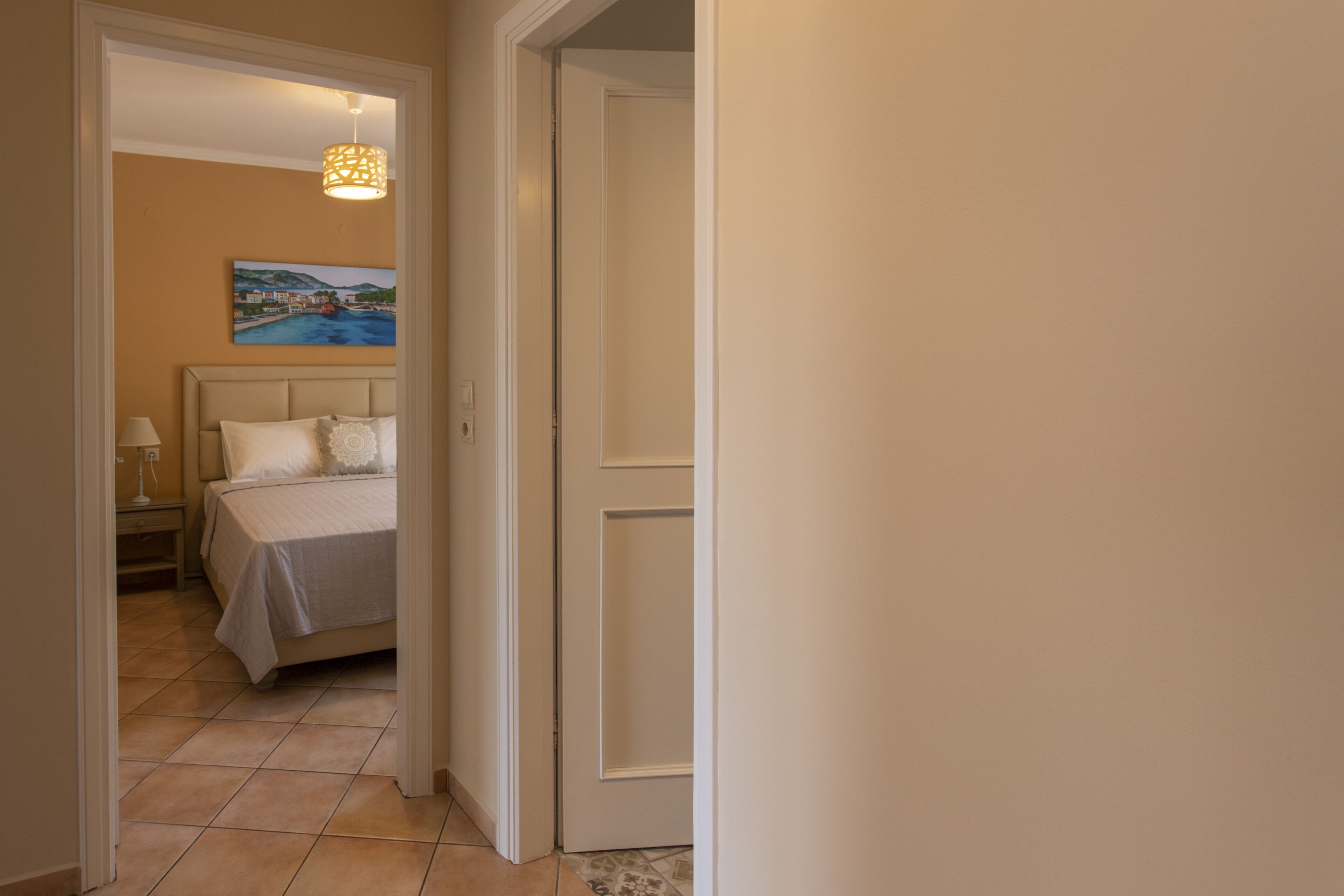 A hotel room with a bed, a painting on the wall, and a door leading to another room.