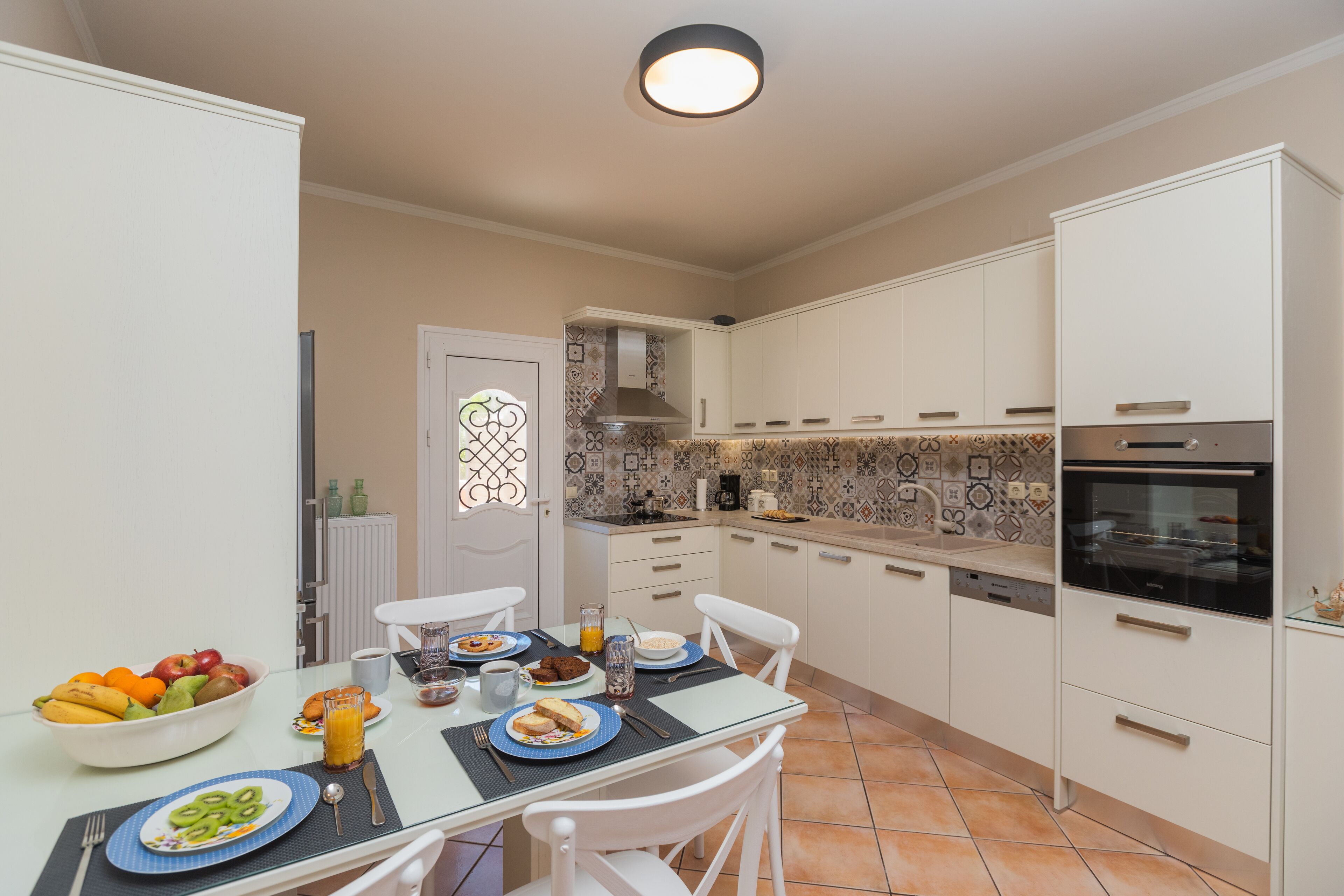Una cocina moderna con alacenas blancas, salpicadero de azulejos y un comedor con mesa de vidrio.