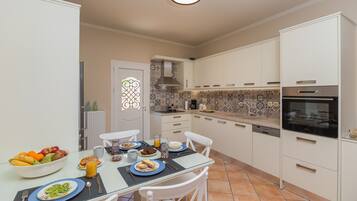 Una cocina moderna con alacenas blancas, salpicadero de azulejos y un comedor con mesa de vidrio.