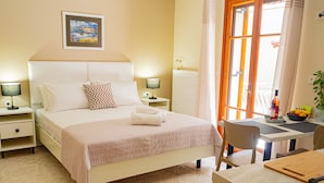 Une chambre d’hôtel avec un lit, des tables de chevet, une table avec une chaise, une fenêtre avec des rideaux et un tableau au mur.