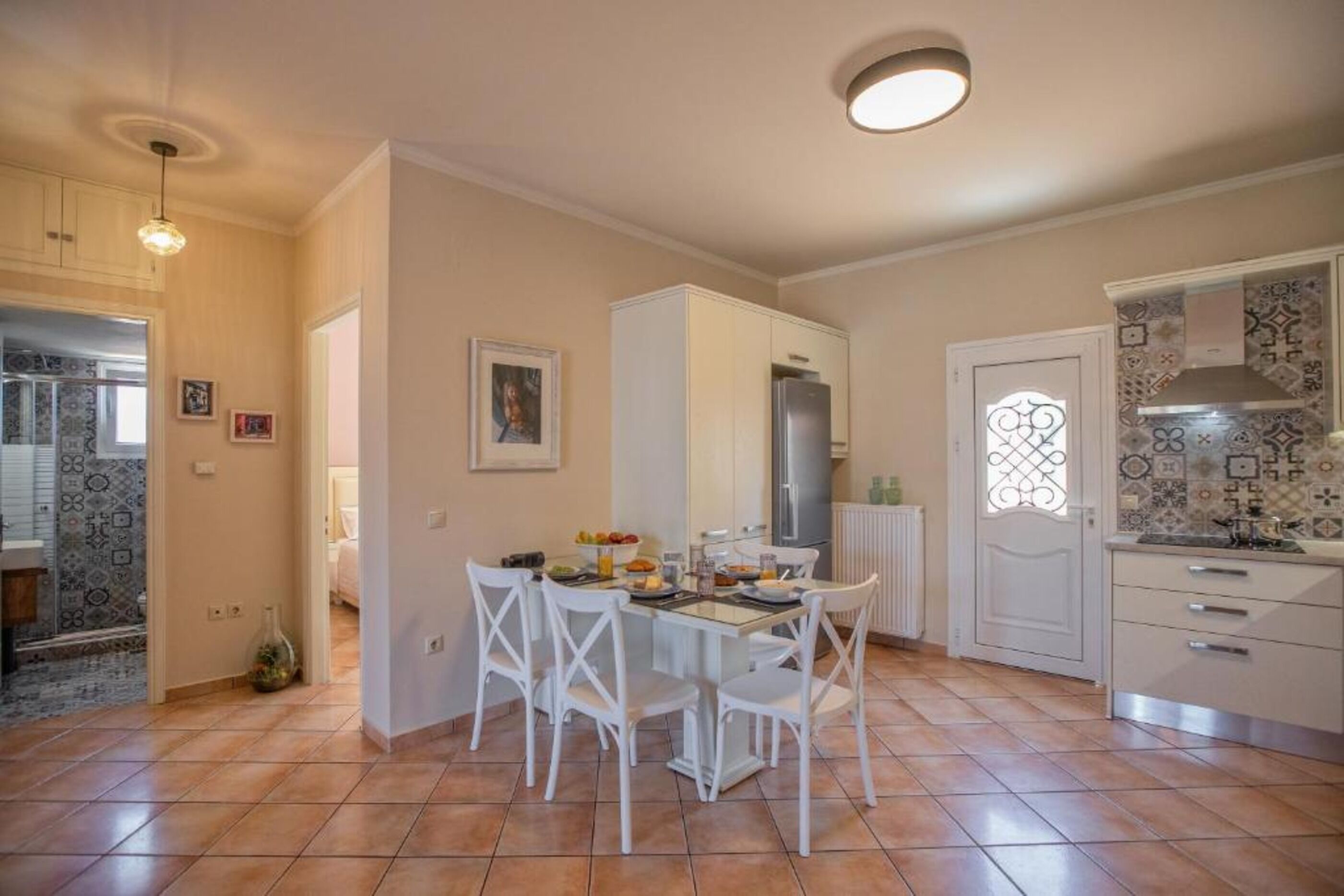 Una cocina con gabinetes blancos, salpicadero de azulejos y un comedor con mesa y sillas.