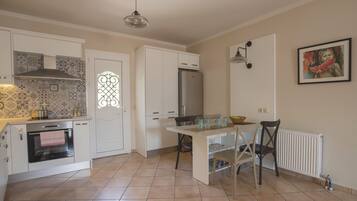 Una cocina con gabinetes blancos, horno empotrado, refrigerador, mesa de comedor con sillas y una lámpara colgante.