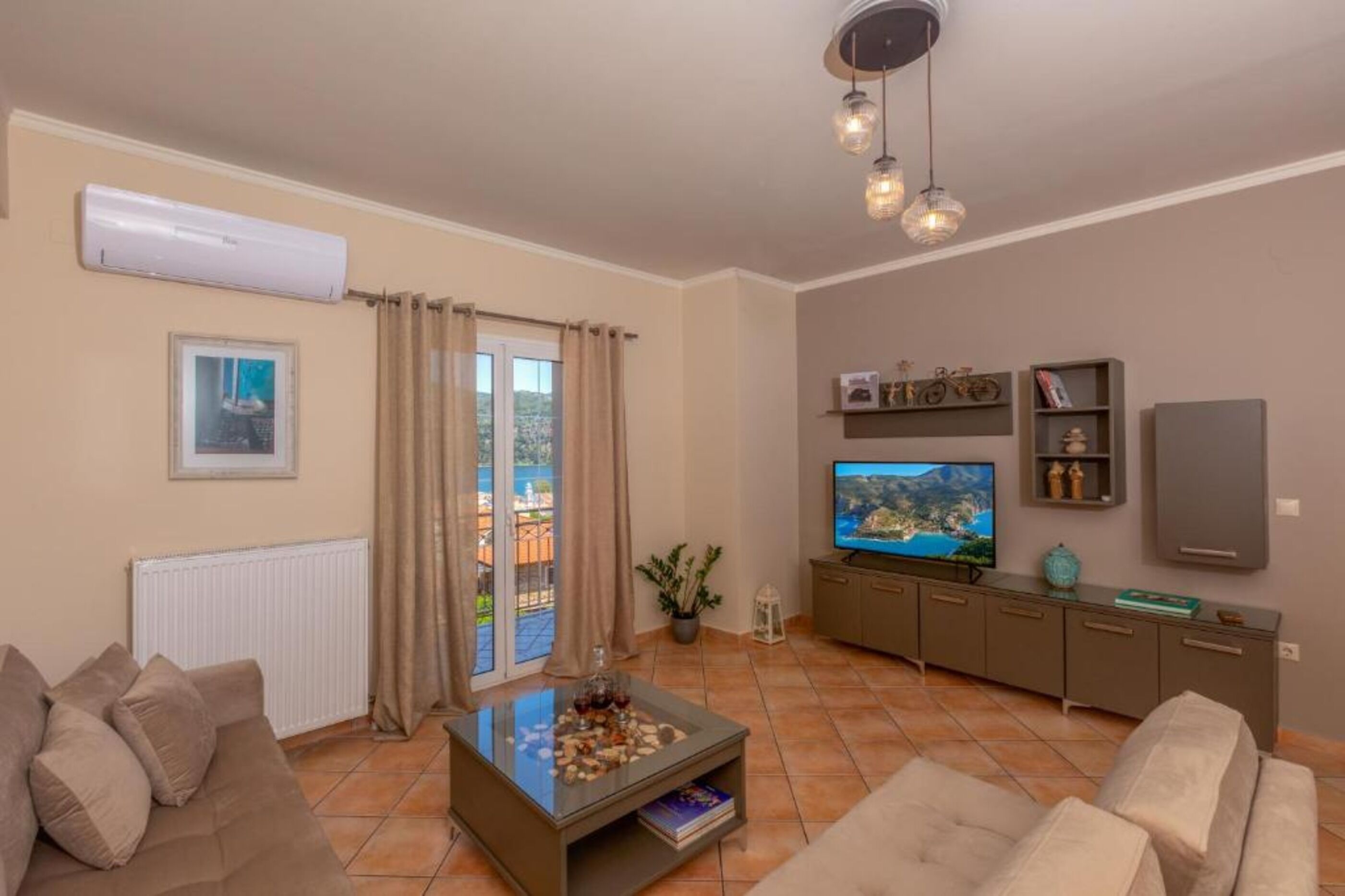 Un salón con sofá, una mesa de centro, televisor y balcón con cortinas.