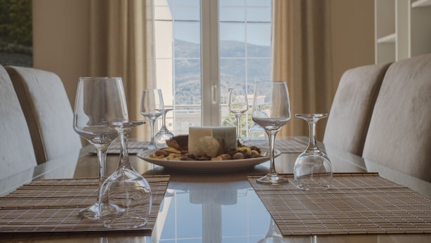 Une table à manger avec une assiette de nourriture et des verres à vin, placée devant une fenêtre donnant sur des collines.