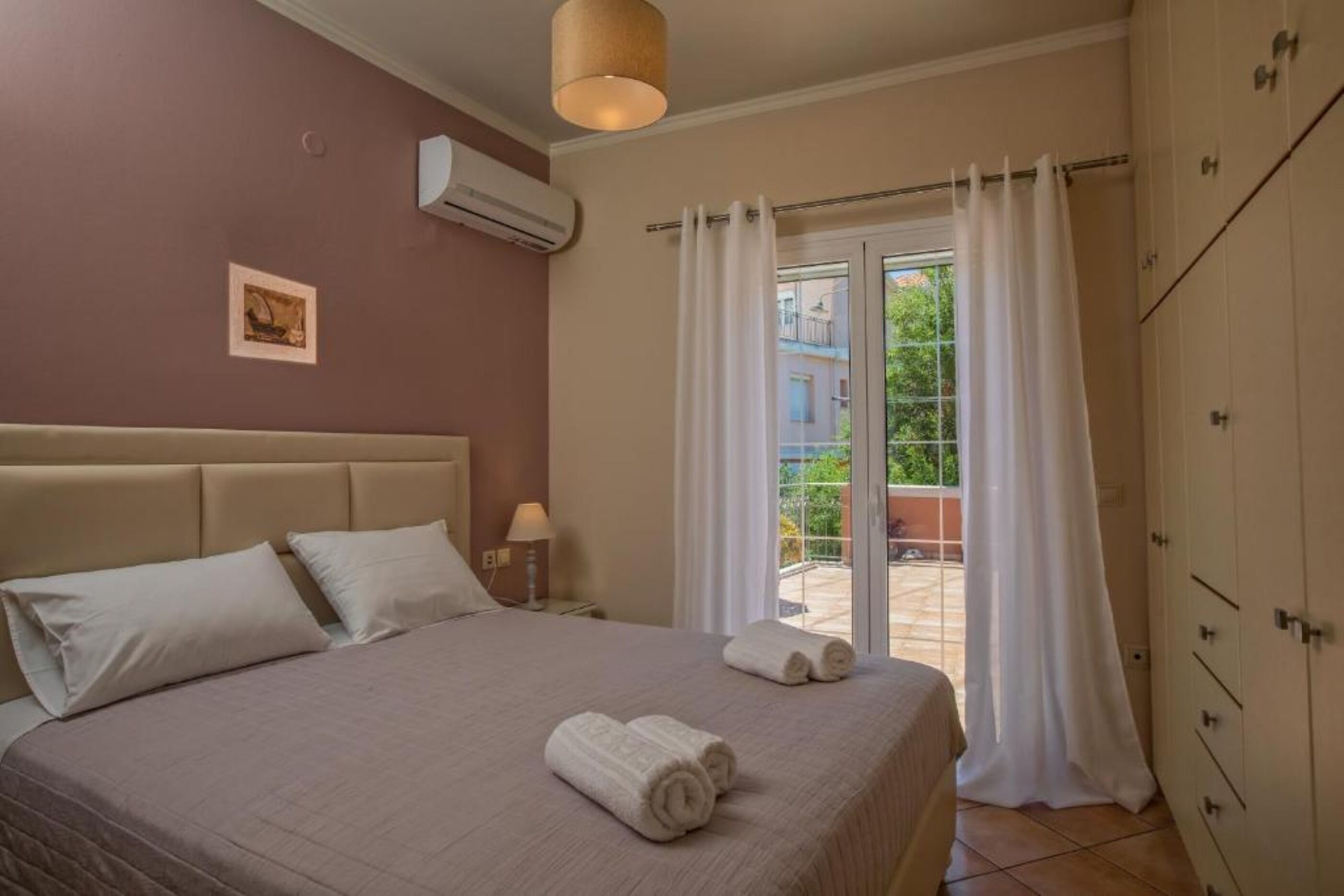 A bedroom with a bed, a nightstand, an air conditioning unit, a window with curtains, and a view of the outside.