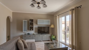 Un salon moderne avec un canapé, une table basse, un téléviseur et une porte-fenêtre coulissante donnant sur un balcon.