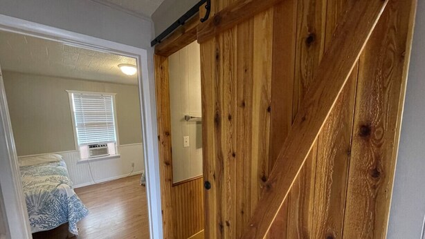 Una habitación con un armario de madera, una cama con colcha azul estampada, una ventana con persianas y una lámpara en el techo.