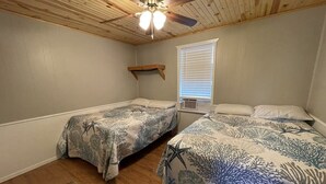 Un dormitorio con dos camas, ventilador de techo, ventana con persianas y una estantería de madera.