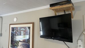 Ein Zimmer mit einem an der Wand befestigten Flachbildfernseher, einem gerahmten Gemälde und einem Holzregal darüber.