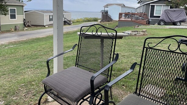 A metal chair with a cushion, a metal table, and a view of a lake and houses in the background.
