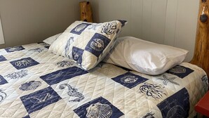 A bed with a quilted bedspread featuring a nautical theme, a white pillow, and a wooden headboard.