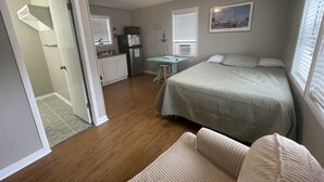 A compact bedroom with a bed, a small desk, and a kitchenette.
