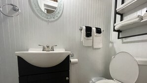 Casa de banho com lavatório branco, armário preto, sanita e porta-toalhas.