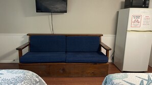 Quarto com sofá azul, televisão fixada na parede e frigorífico com placa de proibido fumar.