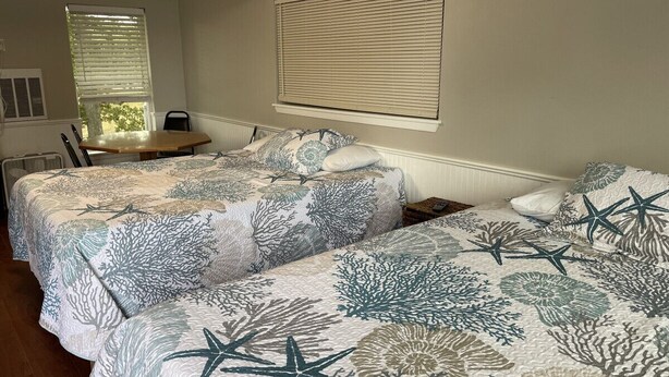 Quarto com duas camas, uma mesa de madeira e uma janela com persianas.