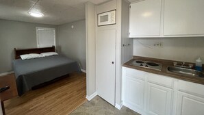 Habitación compacta con cama, kitchenette y una puerta que da a otra habitación.