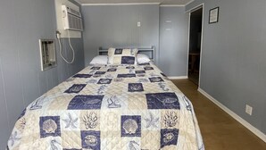 A bedroom with a bed, a wall-mounted air conditioner, and a door leading to another room.