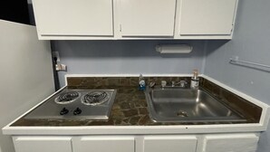 A compact kitchen with two stovetops, a sink, and white cabinets.