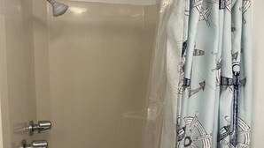 A shower with a handheld showerhead, a glass door, and a curtain with nautical patterns.