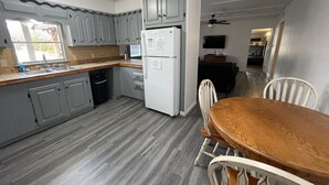 A compact kitchen with grey cabinets, a white refrigerator, and a wooden dining table with white chairs.