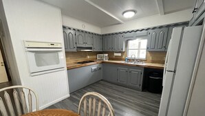 A compact kitchen with white appliances, grey cabinets, and a wooden dining table.
